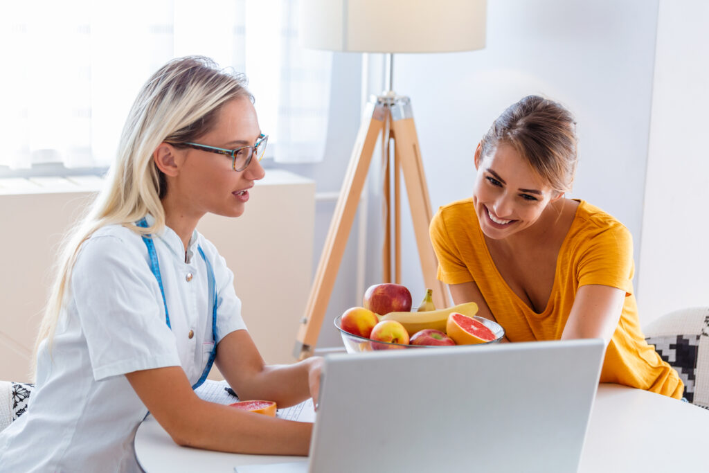 Professional nutritionist meeting a patient in the office and healthy fruits with tape measure, healthy eating and diet concept. Nutritionist desk with healthy fruit, juice and measuring tape.