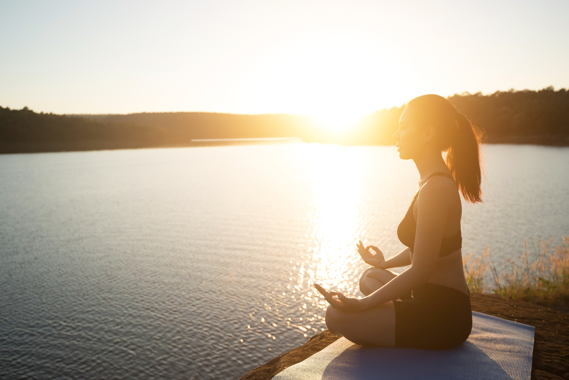 Young healthy woman is practicing yoga at mountain lake during s
