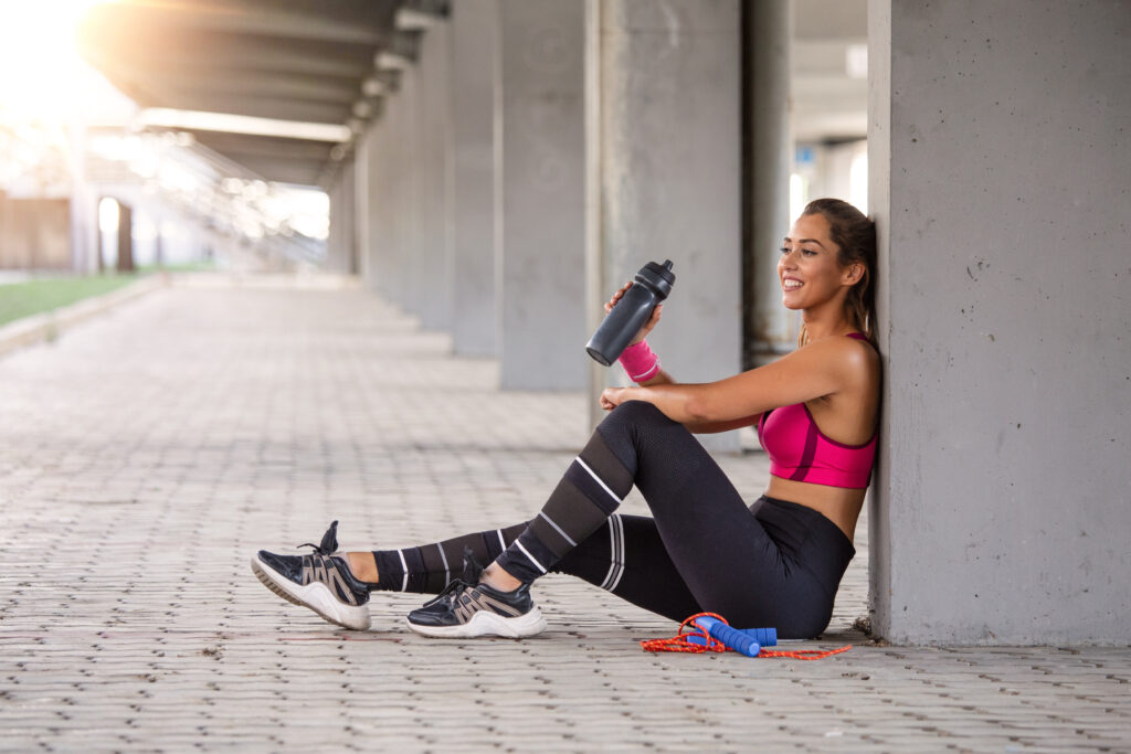 Fitness woman Relaxing after exercise with a whey protein bottle. Relaxing after training. Beautiful young woman looking away while resting after running